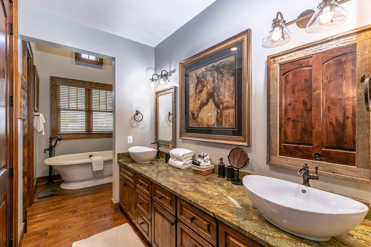 A serene, spa-inspired bathroom is captured here, featuring a vanity with double sinks, a large freestanding soaking tub, and striking framed artwork. Soft natural light fills the space, emphasizing its calming and indulgent qualities.