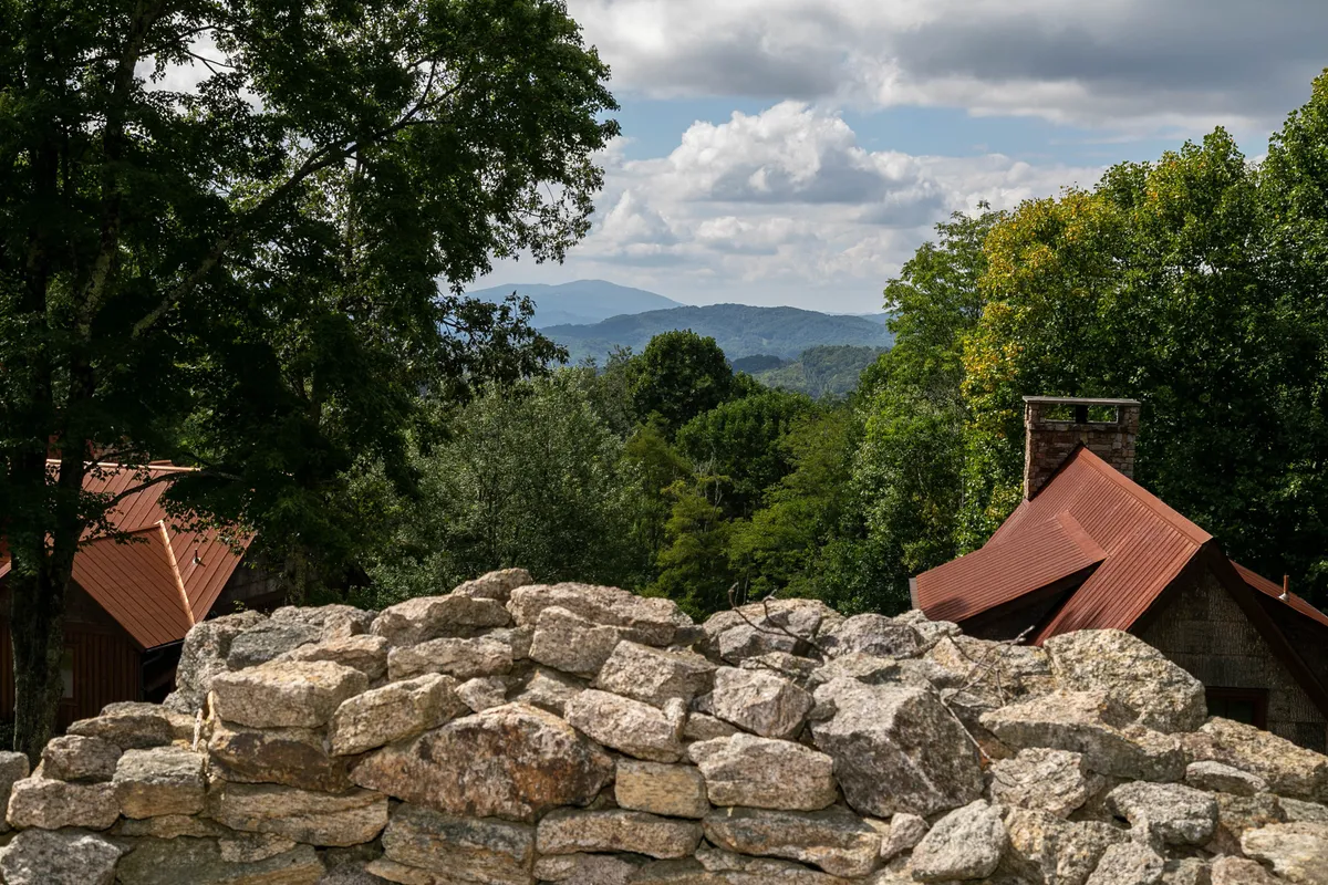 A broad, scenic view over rocky outcroppings and distant mountains, framed by lush trees and the rooftops of rustic lodges. The sky is painted in sunset hues, creating a tranquil yet adventurous atmosphere. The natural landscape suggests opportunities for hiking, biking, and exploring, while the rooftops imply proximity of the lodge to the action.