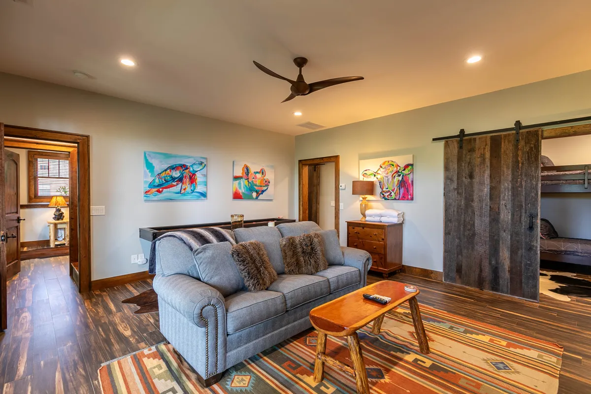 A bright and comfortable sitting area with a plush sofa, engaging artwork, a coffee table, and a sliding barn door. The space is conducive to lounging, playing games, or watching TV with family and friends.