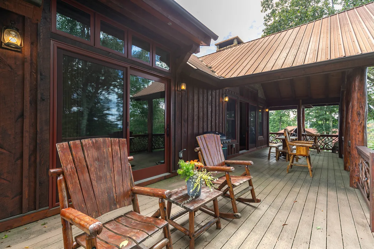 A rustic lodge exterior with wooden rocking chairs and a coffee table topped with flowers on a porch, set against large windows and a wooden structure. The setting is peaceful, inviting guests to relax outdoors and providing an immediate sense of connection to nature.