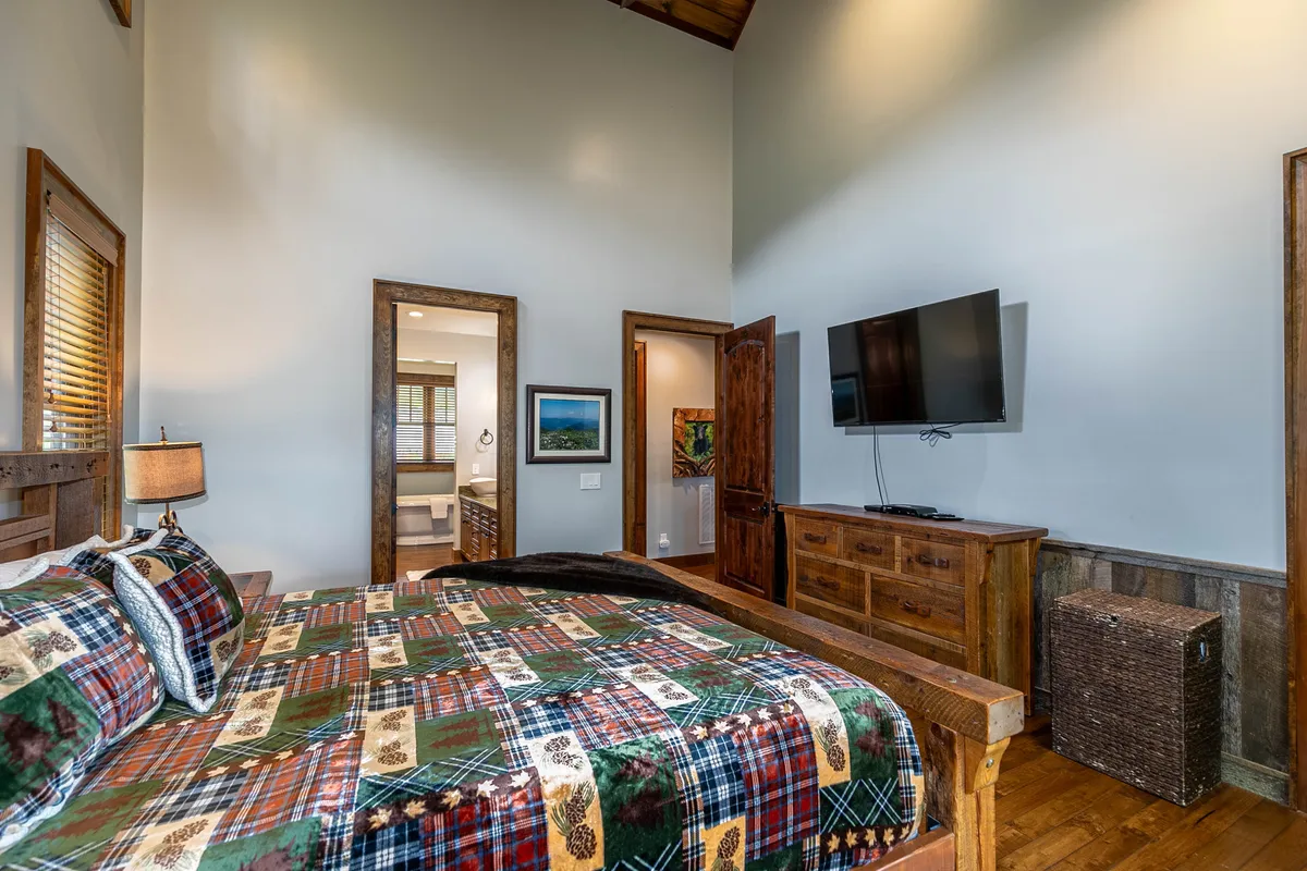 A cozy corner featuring plaid bedding, wooden furniture, a television, and framed artwork. The room is inviting and intimate, ideal for watching movies or enjoying quiet moments.