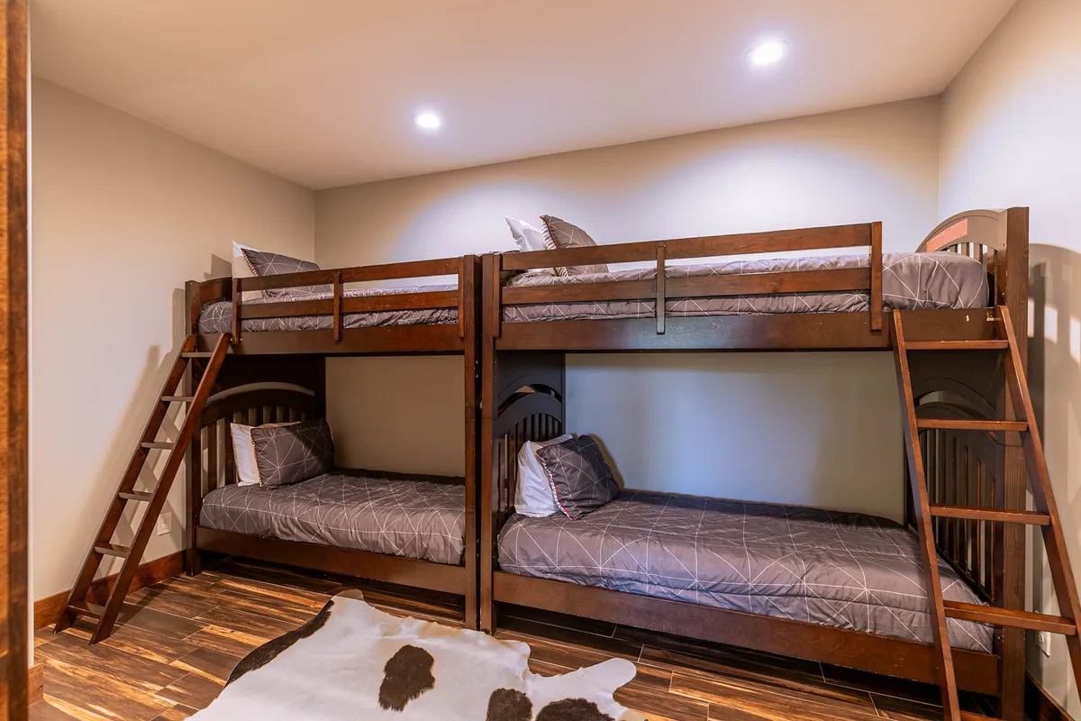 A playful bunk room with two sets of twin bunk beds and a cowhide rug sets a fun, welcoming atmosphere. The room’s design is perfect for kids or friends, offering both comfort and a sense of adventure, clear in the playful bedding and functional layout.